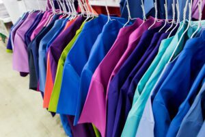 A row of colorful scrubs hanging on a rack at a dry cleaner.