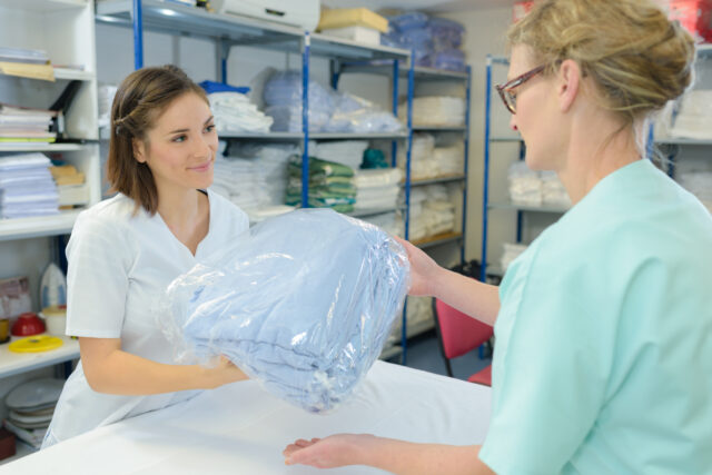 A dry cleaner hands clean laundry to a woman.