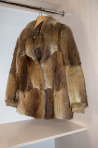 A brown fur jacket is hanging in the closet.