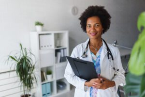 A doctor in white coat with a stethoscope around her neck and holding a clipboard.