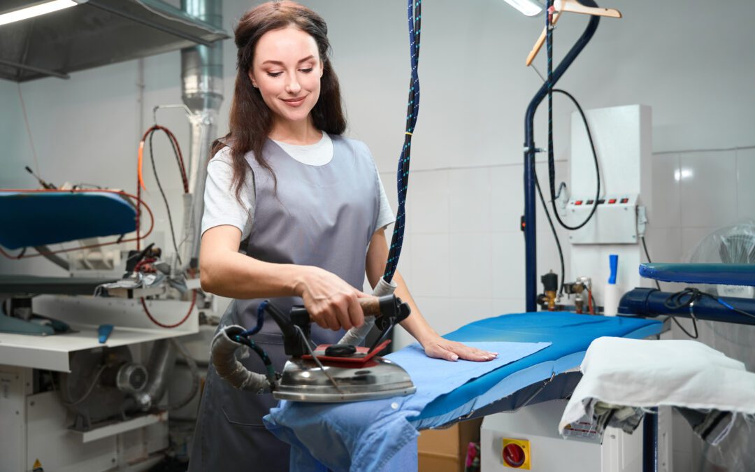 A woman presses a uniform shirt at a dry cleaners.